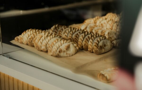Freshly baked empanadas displayed in a glass case, showcasing golden-brown, flaky pastry with intricate crimping, perfect for a savory snack or meal