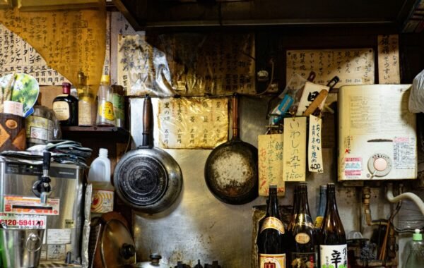 Rustic interior of a traditional Osaka eatery featuring an array of hanging menus, vintage pots, and bottles on shelves, capturing the essence of authentic Japanese dining culture