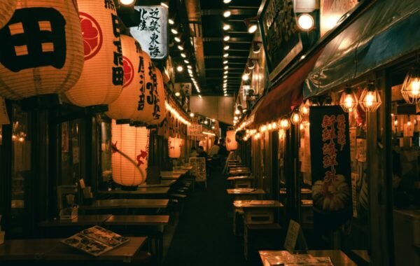 Lively nightlife scene in Osaka featuring lanterns and illuminated signs lining a bustling alley filled with empty tables at traditional restaurants