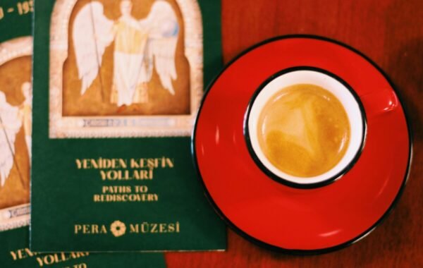 A rich espresso served in a vibrant red cup, accompanied by green guidebooks titled Paths to Rediscovery and featuring art