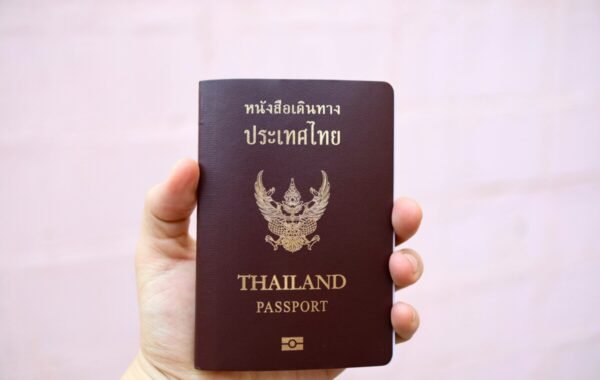 A person holding a Thailand passport featuring gold text and emblem, symbolizing travel and identity