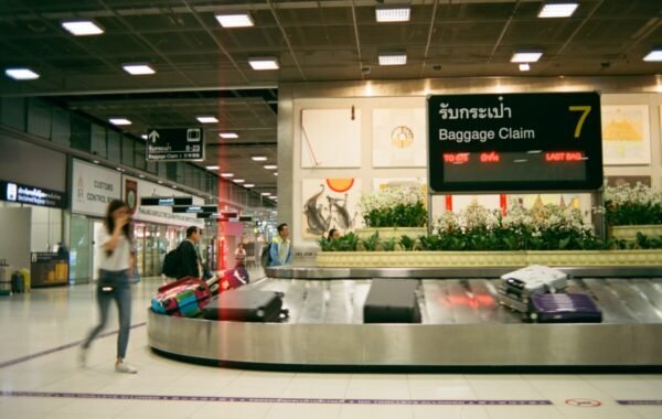 Baggage claim area at a Thai airport featuring travelers retrieving luggage from the carousel, with signs indicating location in both English and Thai