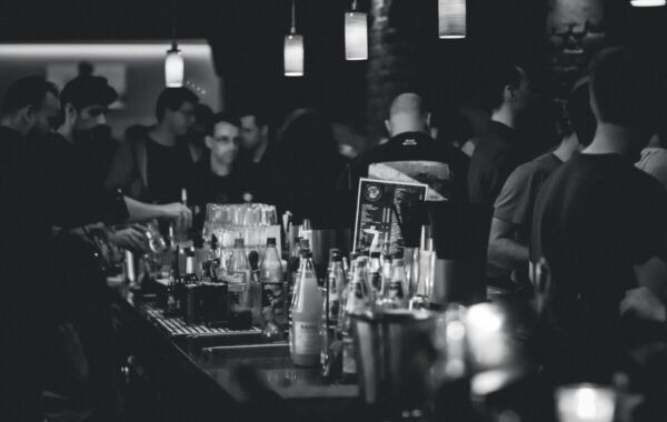 Crowded bar scene in black and white, showcasing various whiskey bottles and drinks being served, highlighting a vibrant nightlife atmosphere