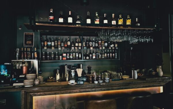 A stylish bar displaying a wide selection of whiskey bottles on shelves, with glasses hanging above and various bar tools on the counter, creating a sophisticated atmosphere for food and drink enthusiasts