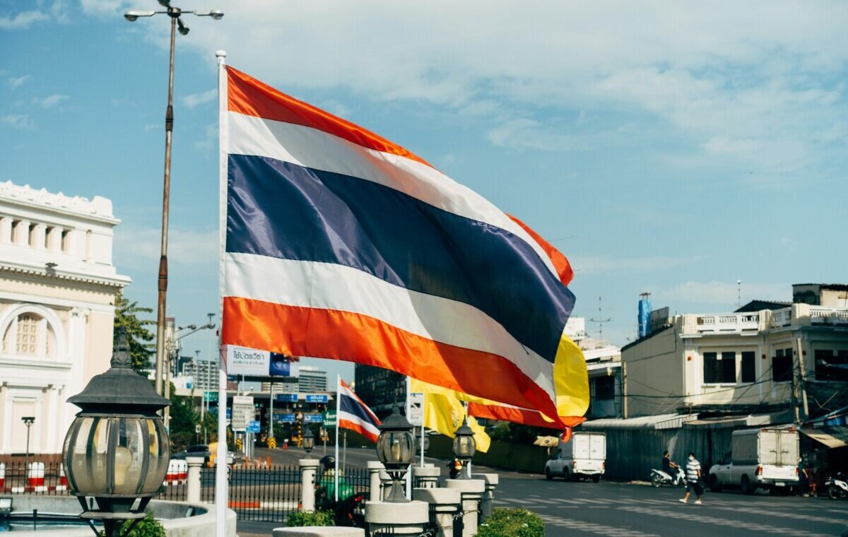 Vibrant Thai flag waving against a clear blue sky, highlighting its red, white, and blue stripes, in a bustling urban setting