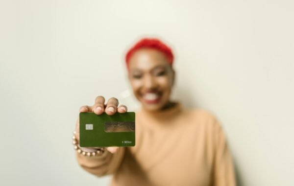 A smiling woman with red hair holds out a green credit card, suggesting side hustles traveling