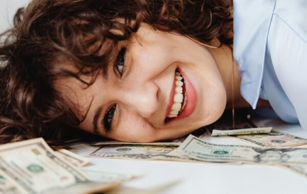 A smiling woman lies on a pile of US dollar bills, suggesting side hustles traveling