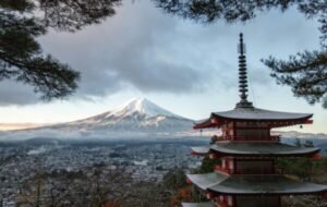 A snow-capped Mount Fuji looms over a city, with a red pagoda in the foreground, perfect for a mount fuji day trip tokyo