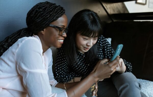 Two women smile as they look at a smartphone, possibly discussing side hustles traveling