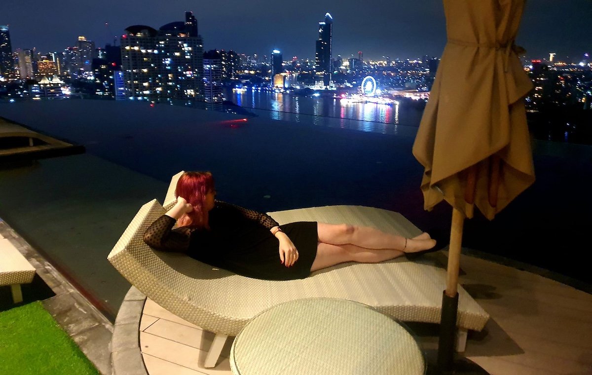 Woman relaxes on a lounge chair overlooking a city skyline at night, enjoying the advantages of digital nomad life