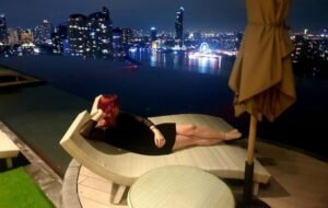 Woman relaxes on a lounge chair by an infinity pool overlooking a city skyline at night, enjoying the advantages of digital nomad life